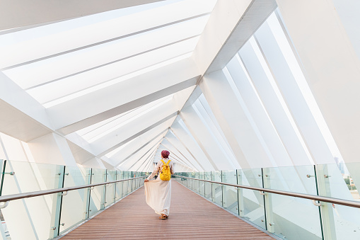 Happy woman tourist walking and admiring the unique interior of the pedestrian bridge over the water channel in Dubai, UAE