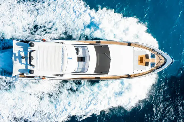 View from above, stunning aerial view of a luxury yacht cruising on a blue water creating a wake. Sardinia, Sardinia, Italy.