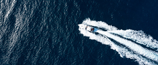 View from above, stunning aerial view of a luxury yacht cruising on a blue water creating a wake. Sardinia, Sardinia, Italy.