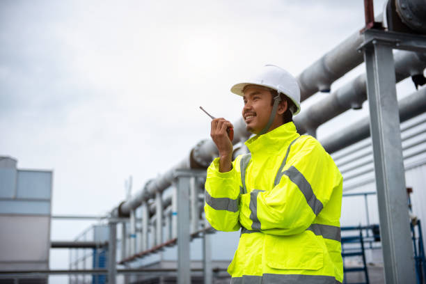 Male Industrial Engineer in the Hard Hat and Wear Yellow Safety Jacket while Standing outdoor at the work plant stock photo