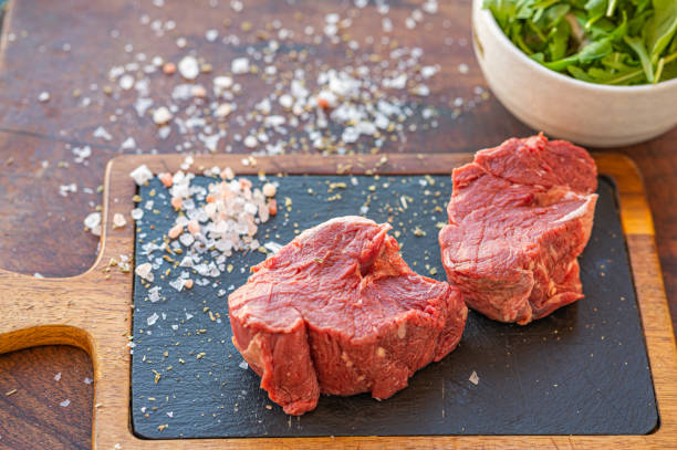 Raw Hereford grass fed beef tenderloin Raw Hereford grass fed beef tenderloin on black slade board with salt, knife and a cup of rocket salad grass fed stock pictures, royalty-free photos & images