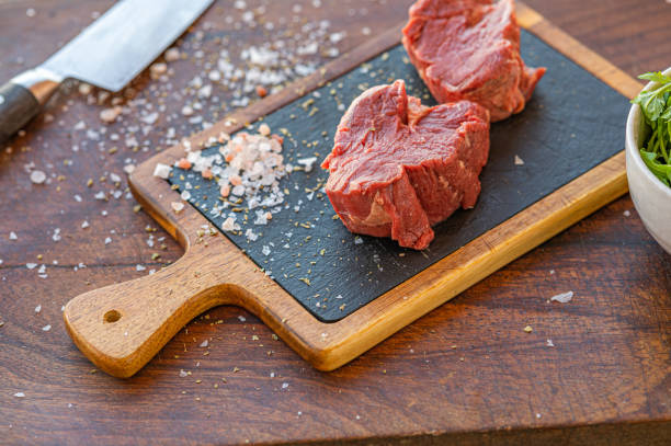 Raw Hereford grass fed beef tenderloin Raw Hereford grass fed beef tenderloin on black slade board with salt, knife and a cup of rocket salad grass fed stock pictures, royalty-free photos & images