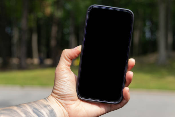 istock Tattooed wrist holding mobile phone outdoors with black blank screen 1333072987