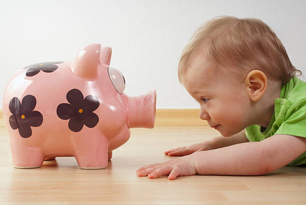 child looks at a piggy bank Child lying on the floor in front of a piggy bank gegenüber stock pictures, royalty-free photos & images