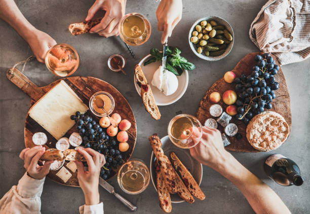 Flat-lay of people drinking wine eating gourmet snacks Flat-lay of human hands drinking wine eating fresh cheese fruits bread wine snacks over grey concrete table background, top view. Gathering, celebrating, wine tasting and party concept cheese wine food appetizer stock pictures, royalty-free photos & images