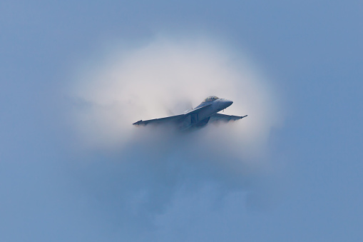 Ocean City, USA - June 12, 2011: F/A-18 Super Hornet speed pass with spectacular visible vapor cone which is effect called Prandtl–Glauert singularity when plane travels with subsonic speed in specific weather condition.