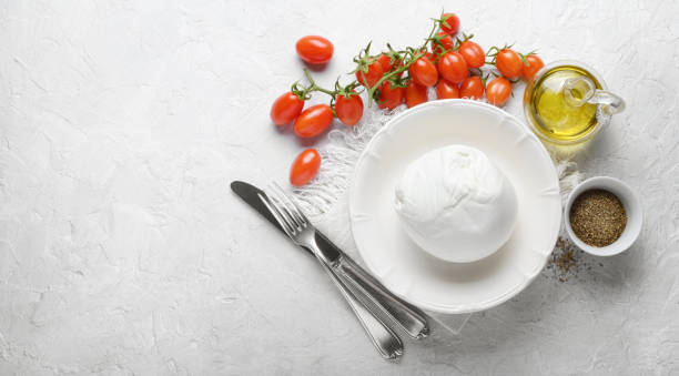 Buffalo mozzarella, cherry tomatoes, extra virgin olive oil and oregano on white plaster background, top view, space for text.