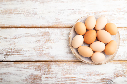 Pile of colored chicken eggs on plate on a white wooden background. top view, flat lay, copy space.