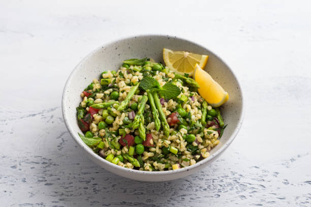 traditioneller nahöstlicher oder arabischer tabbouleh-salat aus bulgur, tomaten, spargel, grünen erbsen und gemüse mit einer halben zitrone auf hellgrauem hintergrund, dre. gesundes hausgemachtes veganes essen - tabbouleh vegeterian food middle stock-fotos und bilder