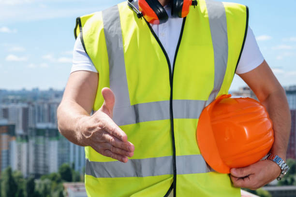 istock Builder holds out one hand for a handshake and the other holds an orange helmet 1333096205