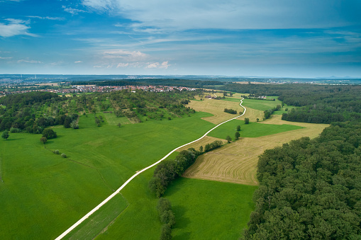 Lonely path leads past the edge of the forest. Rural area in germany. Small village in the background. Aerial view.