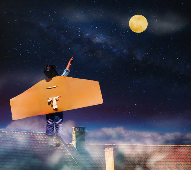 istock Boy with cardboard wings on roof point to sky 1333101191