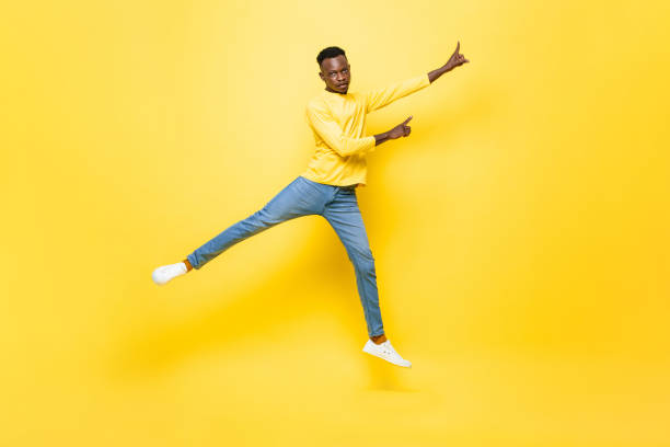 istock Young energetic African man jumping and pointing hands up on isolated yellow studio background 1333101716