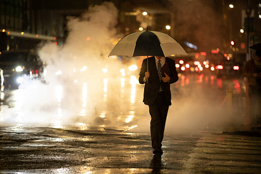 Man in suit walking with an umbrella in the rain.