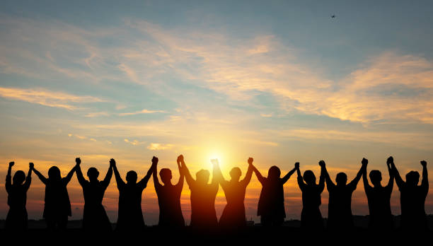 silhouette de l’équipe d’affaires du groupe faisant les mains hautes sur la tête dans le ciel du coucher du soleil - societal photos et images de collection