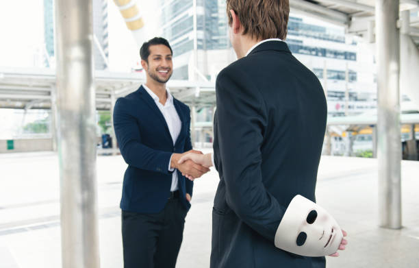 Two business making handshake a deal but holding white mask in his hand dishonest cheating agreement Two business making handshake a deal but holding white mask in his hand dishonest cheating agreement. Treachery risk, Faking and betray business partnership concept. cheesy grin stock pictures, royalty-free photos & images