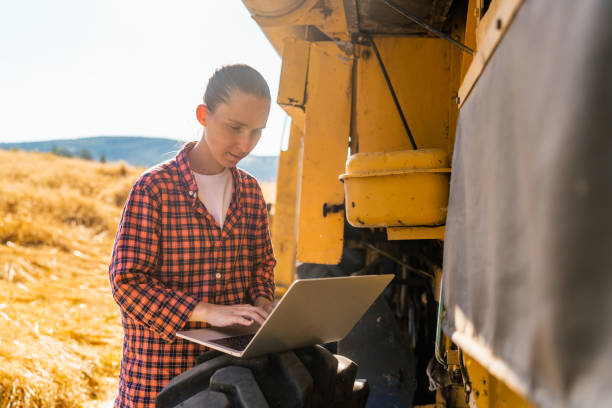 istock Female farmer using laptop next to combine harvester machine 1333123955