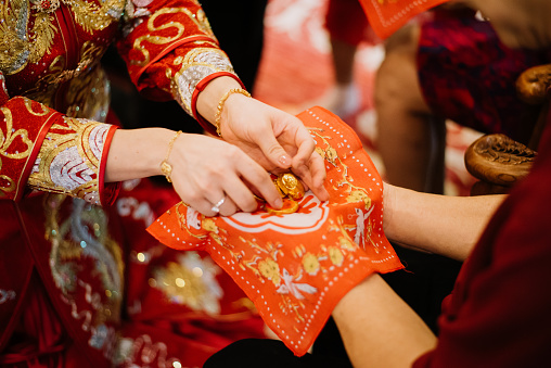 Chinese bride in traditional costume receiving jewelry from elderly during tea ceremony in wedding
