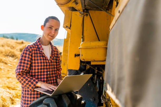 istock Female farmer using laptop next to combine harvester machine 1333125790