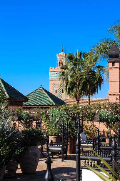 Moroccan Riad with flowers, palm trees, original lamp and view of the mosque of al-Koutoubia. Moroccan Riad with flowers, palm trees, original lamp and view of the mosque of al-Koutoubia. Marrakech, Morocco marrakesh riad stock pictures, royalty-free photos & images