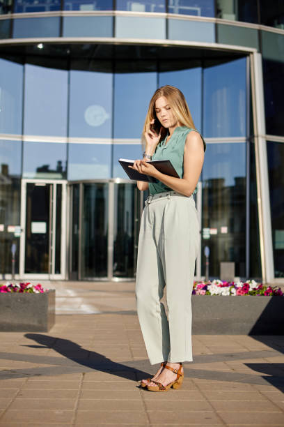 istock Woman with notebook talks by smartphone near office center. 1333136081