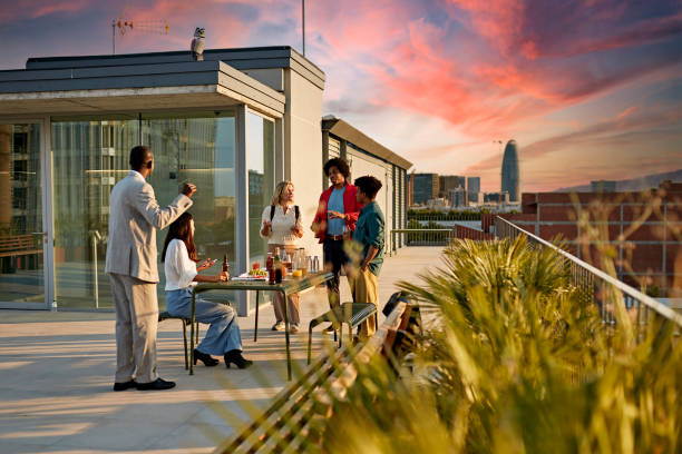 Office Workers Enjoying Drinks and Snacks on Rooftop Deck Full length view of diverse group socializing after work with dramatic sky and Barcelona cityscape in background at sunset. rooftop deck stock pictures, royalty-free photos & images