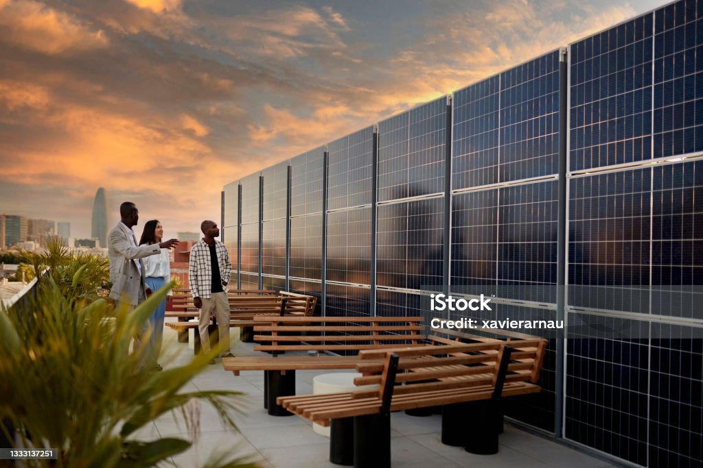 Broker and Prospective Buyers Admiring Solar Energy System Real estate agent and couple standing on rooftop of environmentally aware office building with dramatic sky and Barcelona cityscape in background at sunset. Sustainable Resources Stock Photo