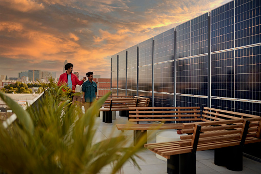 Couple and broker standing on rooftop deck of office building admiring commitment to renewable energy with dramatic sky and Barcelona cityscape in background.
