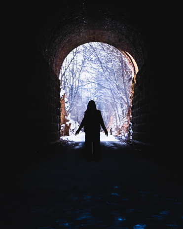 Silhouette of woman standing in former railroad tunnel converted into recreational area in winter; snow covered trees in background