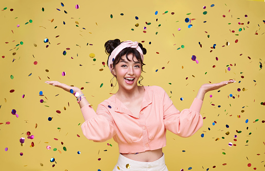 Beautiful happy Asian teen woman at celebration party with confetti falling. New Year eve or Birthday celebrating concept.