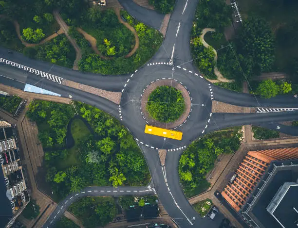 Drone images of city bus driving through a roundabout in "Klimakvarteret", the Climate Resilient Neighbourhood in Østerbro. This area is Copenhagen´s first district to adapted to climate change and to withstand the large volumes of water expected with more extreme weather conditions. The solution is to build large interconnected reservoirs collecting rain water from the city streets, roofs and surfaces. The reservoirs have resulted in large green, recreative areas which invite for picnics, playgrounds and new habitats for urban wildlife supporting biodiversity.