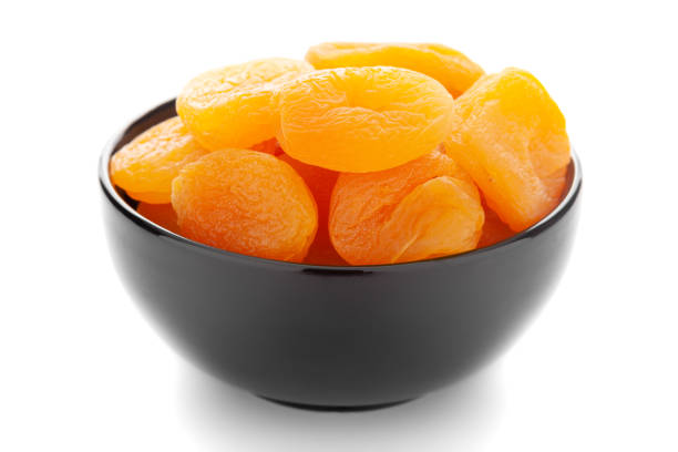 nahaufnahme der orangefarbenen getrockneten aprikose (prunus armeniaca) in einer schwarzen keramikschüssel über weißem hintergrund. - dried apricot stock-fotos und bilder