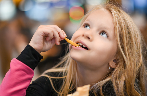 Little girl eating french fries in fast food cafe.