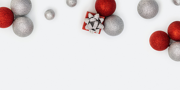Christmas composition with silver and red christmas balls and gift box with surprise on white background with copy space. New Year holiday banner with bright celebration decorations. Flat lay, top view