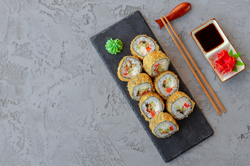 Japanese sushi tempura roll served on black stone plate, close up