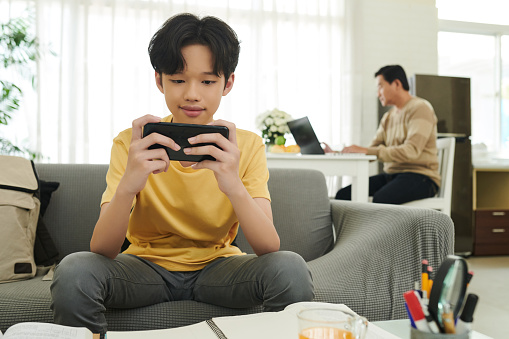 Smiling teenage boy using application or playing videogame on his smartphone