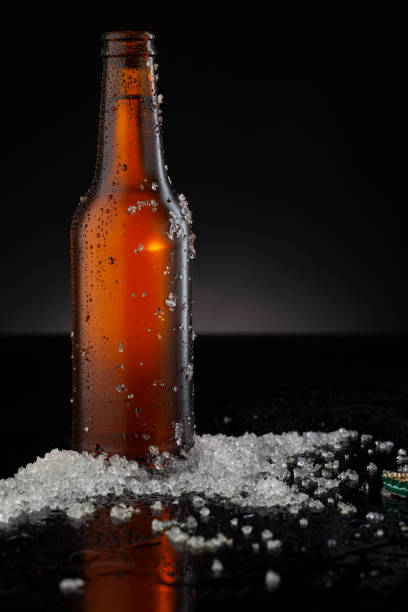 istock Ice Cold Brown Beer Bottle Covered with ice and water drops - condensation. Blank for drink beverage product design mock-up.  Standing on black table with dark - black background. 1333150985