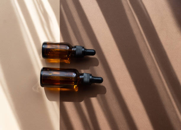 istock Mock-up of two glass dropper bottles lying parallel on abstract two-color background. Shadows from sun's rays, in form of stripes, fall on. Concept of beauty industry 1333151167
