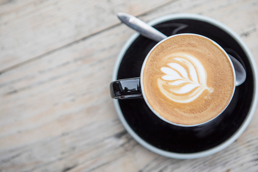 Decorative leaf pattern in the milk of a flat white coffee, on a rustic wooden surface