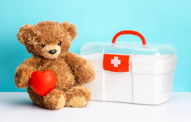Teddy bear with heart and first aid kit on green background