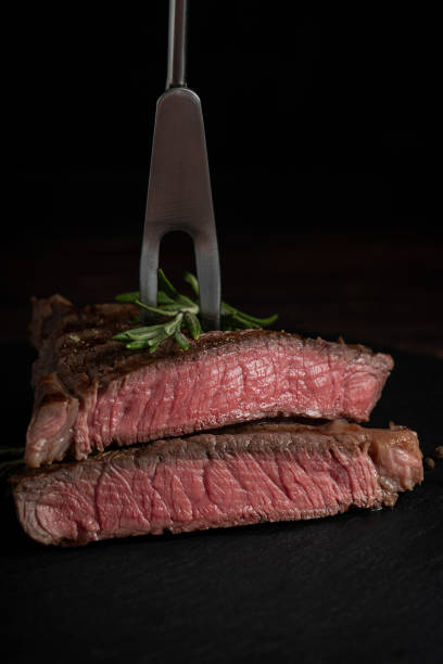 seitenansicht von geschnittenem steak mittlerer röstung aus rindfleisch mit frischem rosmaringewürde - veal raw meat pink stock-fotos und bilder