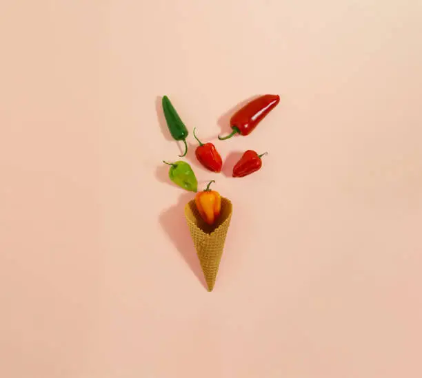 Photo of Jalapeno and habanero hot chili peppers in ice cream cone. Minimal flat lay composition on pastel pink background