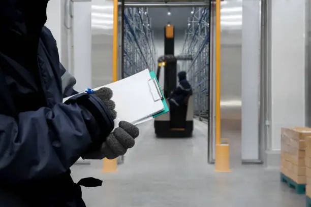 Hand of worker with clipboard checking goods in freezing room or warehouse