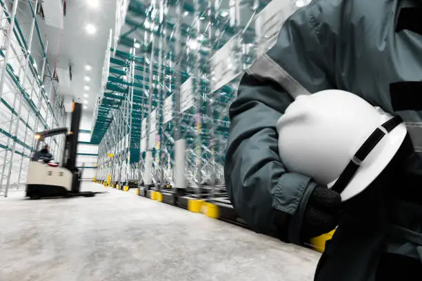 Safety hardhat for dangerous accident protection in warehouse during work. Cold room storage and freezing warehouse with stacker truck inside moving.
