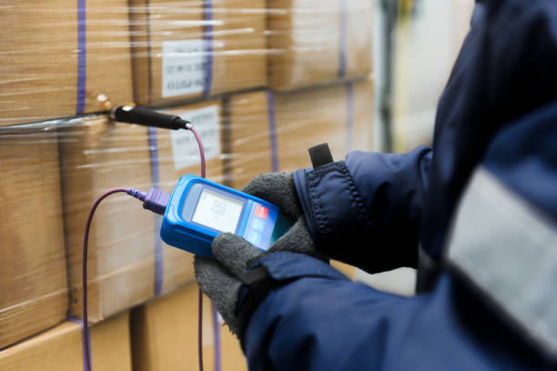 hand des arbeiters mit thermometer zur temperaturmessung in den warenboxen mit fertiggerichten nach dem import im kühlraum oder lager für den temperaturraum halten - kälte stock-fotos und bilder