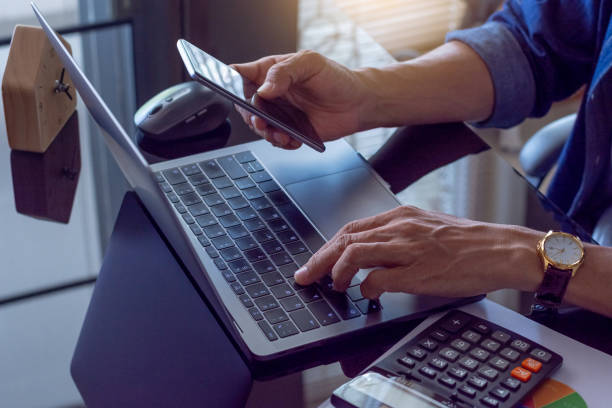 istock Casual business man hand using mobile smart phone and typing on laptop computer keyboard with calculator and data graph paper on the mirror table 1333163796