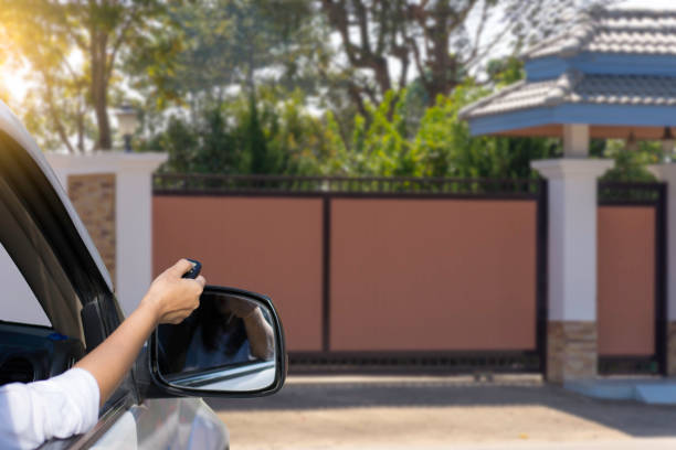 The electric door and home remote control in concept. Woman in car, hand using remote control to open the automatic gate with  home blurred background when arrived home. The electric door and home remote control in concept. gate stock pictures, royalty-free photos & images