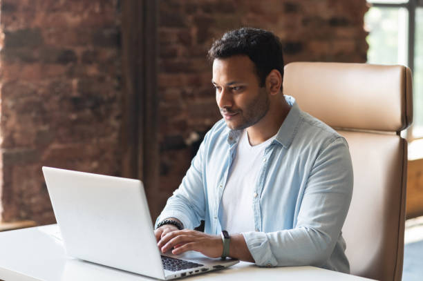 istock Indian developer guy is working with a laptop sitting at the desk indoors 1333167008