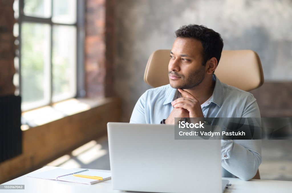Serious concentrated clever indian freelancer guy using laptop for searching Serious concentrated clever indian freelancer guy using laptop for searching, looking away lost in searching ideas for startup, a thoughtful millennial work remotely at home Contemplation Stock Photo