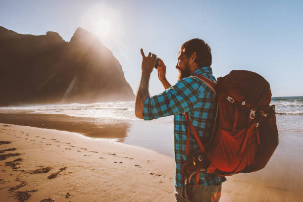 istock Man backpacker taking photo using smartphone camera travel blogger influencer in Norway summer trip outdoor vacation Kvalvika beach 1333170245